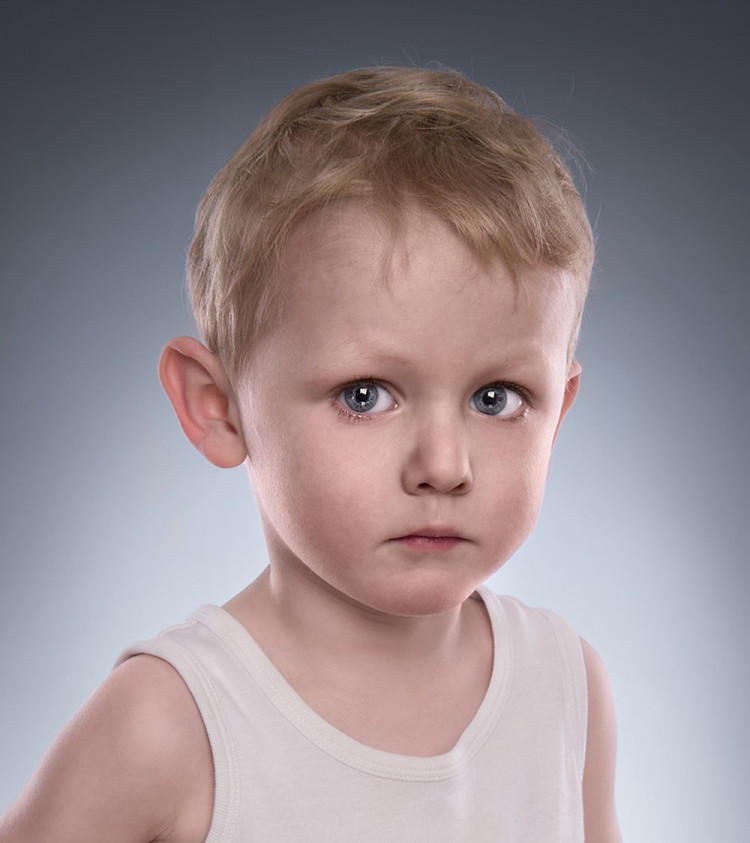 Børneportræt af dreng med store blå øjne, der ser lidt alvorlig ud