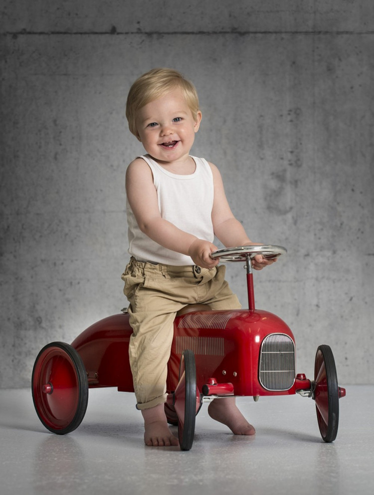 Billede af glad lille dreng, der kører på en rød retro legetøjsbil