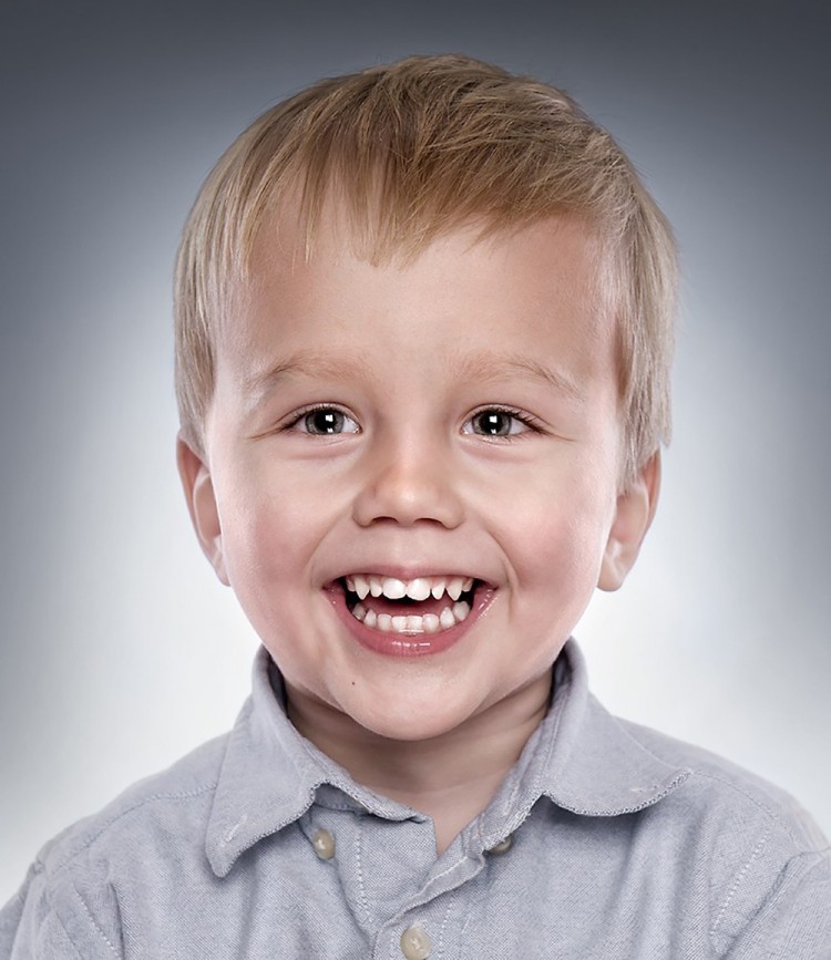 Klassisk børneportræt af dreng, der smiler stort – blå baggrund