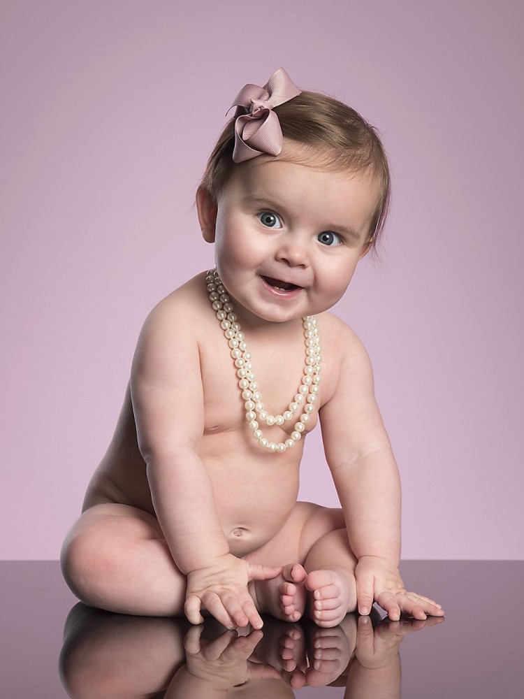 Fin lille pige med perlekæde om halsen og lyserød sløjfe i håret til månedsfotografering