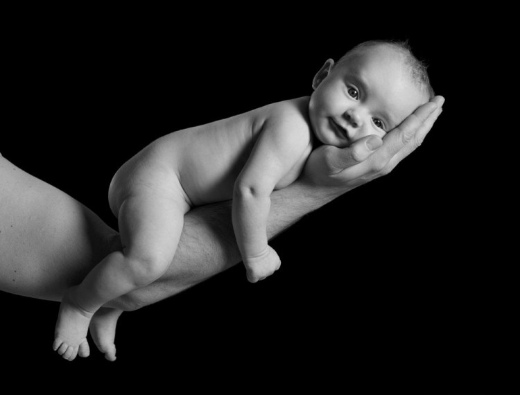 Lille baby ligger og slapper af på fars arm, sort-hvidt billede med sort baggrund