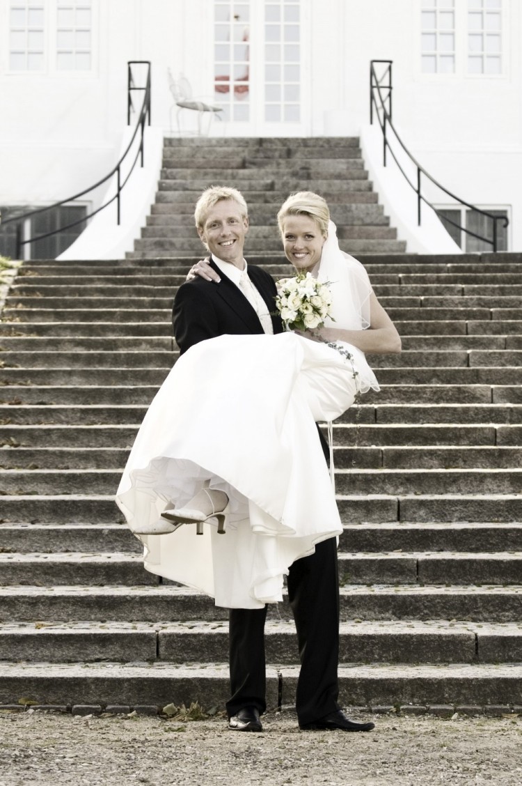 Brudgom bærer sin brud foran trappe til slot – bryllupsfoto
