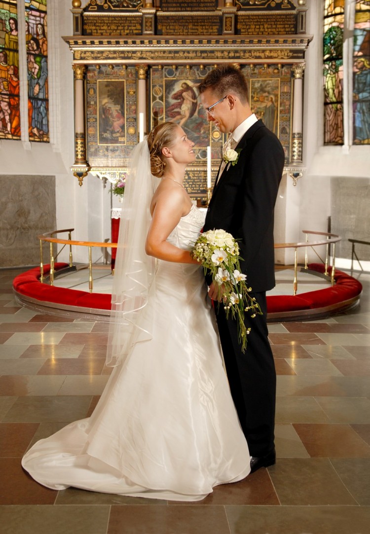 Foto af brudepar foran alteret – står med siden til og kigger hinanden i øjnene