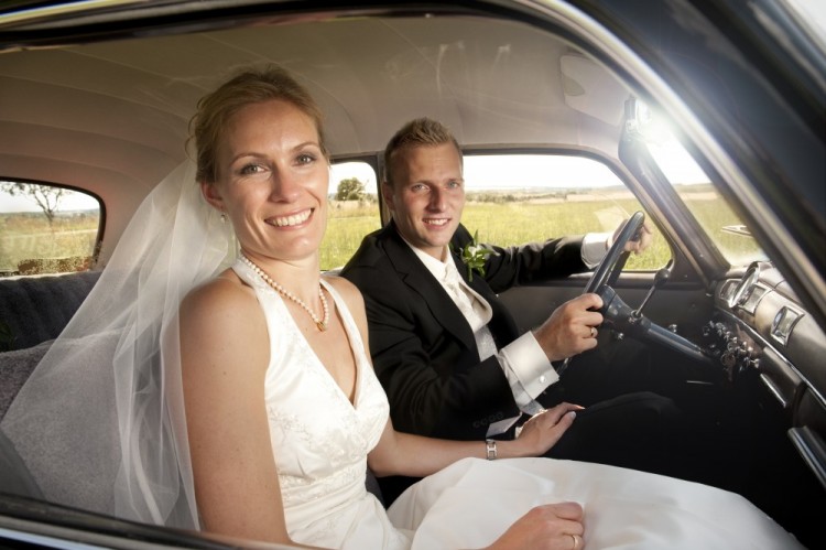 Bryllupsbillede af brudgom, der kører sin brud hjem i veteranbil