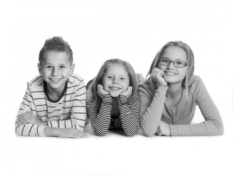 Børneportræt af tre søskende, der ligger ned ved siden af hinanden med ansigterne mod kameraet