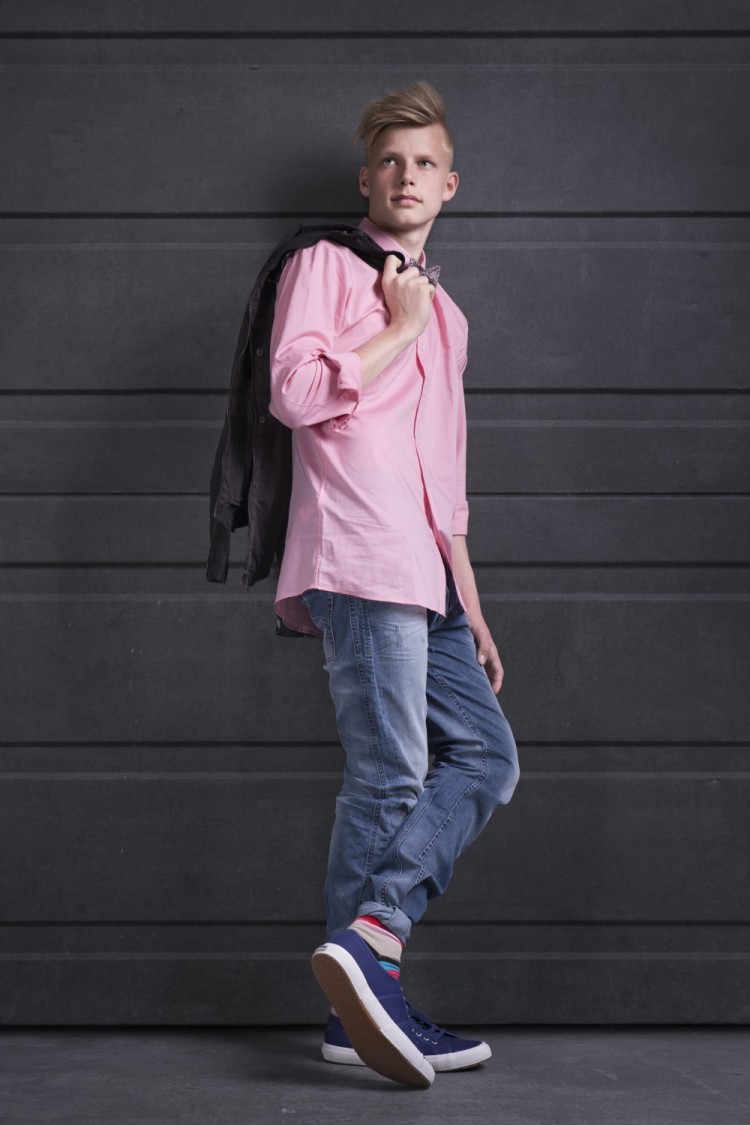 Billede af konfirmand med lyserød skjorte på læner sig op ad væg med jakken over skulderen