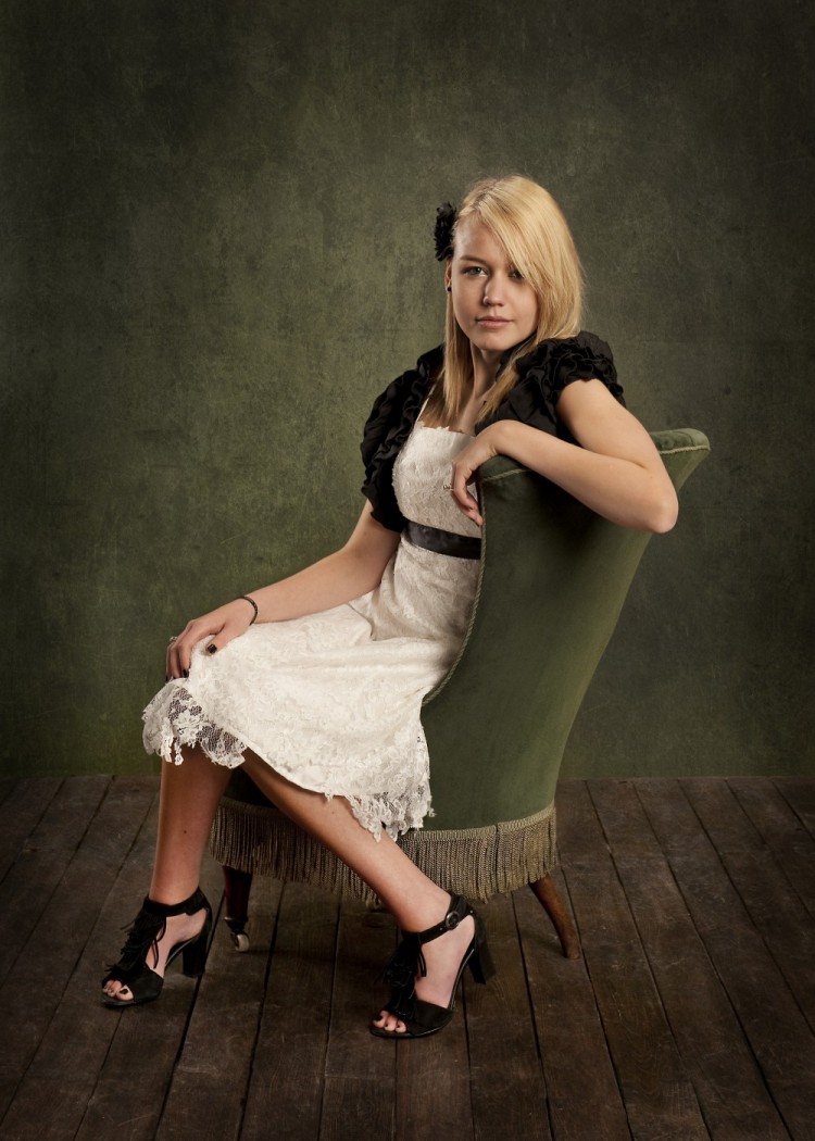 Konfirmationsbillede af pige med hvidt og sort tøj, hun sidder i en gammel grøn velourstol