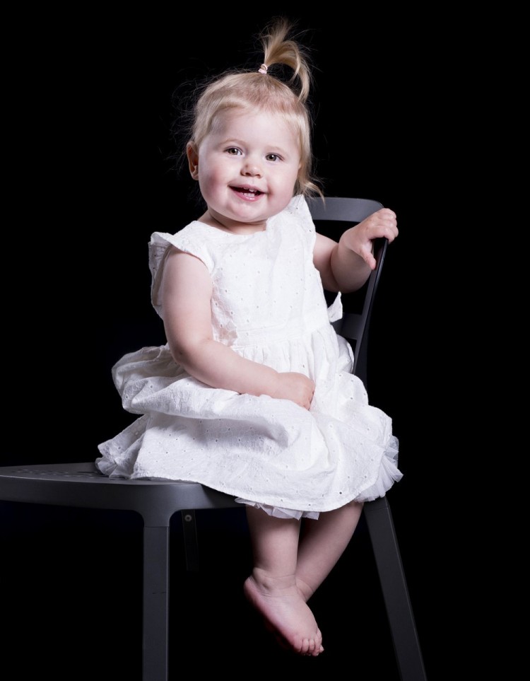 Børneportræt af kær lille pige i fin blondekjole siddende på en stol, hun er omkring 1 år